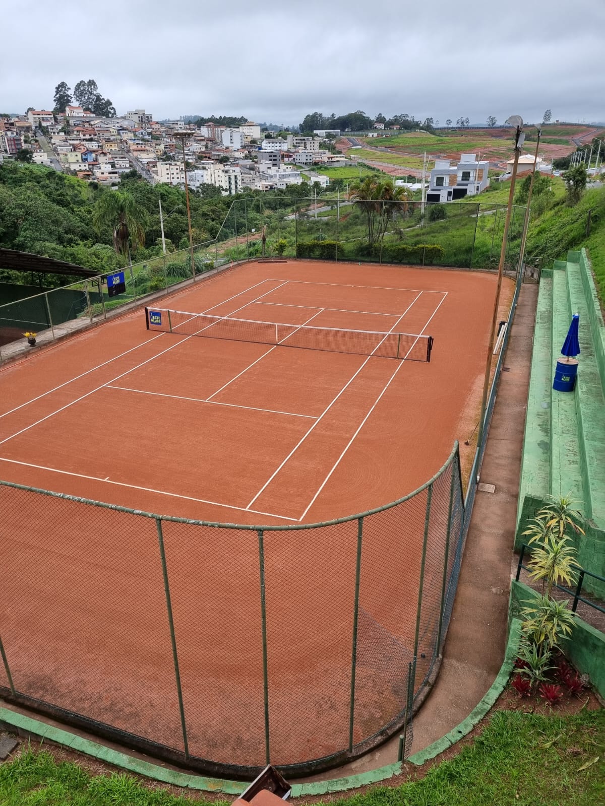 Quadra de tênis de saibro do Oeste Clube com arquibancadas verdes