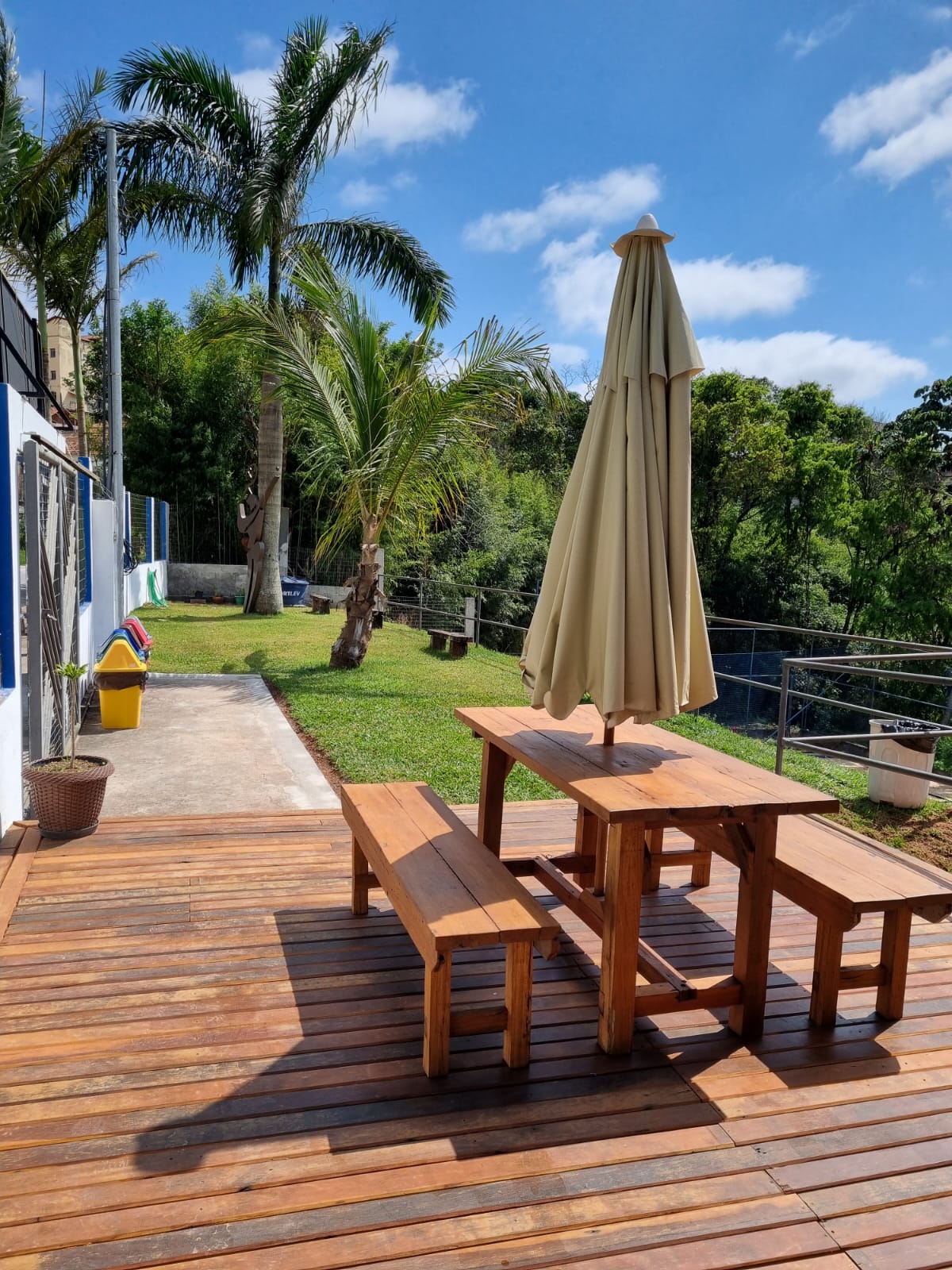 Deck de madeira com mesa, bancos e guarda-sol na área social do Oeste Clube